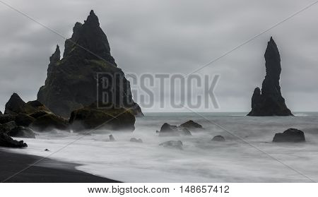 Reynishverfisvegur Reynisfjara black sand beach with rocks ocean and dark rain and storm clouds near the village of Vik in Iceland.
