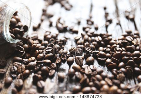 Coffee beans are on the wooden textured table with the glass jar