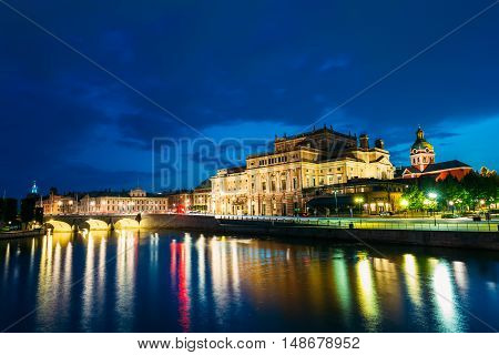 Stockholm, Sweden. The Scenic Night View Of Illuminated Royal Swedish Opera Theatre And Norrbro Arch Bridge Over Norrstrom Waterway With Lights Reflections In The Water Under Dramatic Blue Sky.