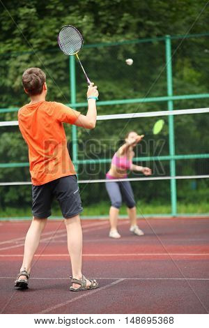 Boy with her mother play badminton on the playground, view from the back
