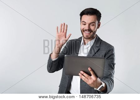Hallo my friend. Young handsome man smiling and having conversation on his tablet while standing against white background.