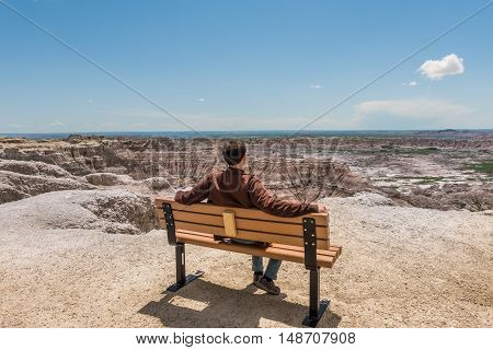 Man sitting on bench looking at view of eroded Badlands canyons in national park
