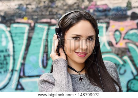 Portrait of young beautiful woman with black headphones against graffiti wall. Outdoors. Urban concept.