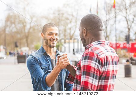 Two men giving a friendly handshake. A black man meeting his middle eastern friend and greets him in London. Friendship and lifestyle concepts.