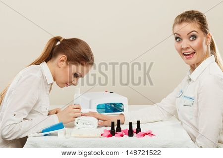 Relaxing time and wellness day concept. Blonde elegant woman visiting professional manicurist salon. Beautician makes perfect nails to client.