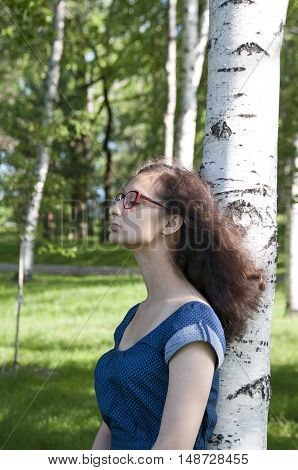 Girl in blue dress near a birch closed her eyes
