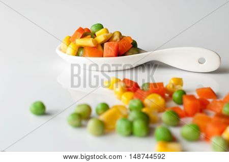 Vegetables three colors carrots kernels peas in spoon white background