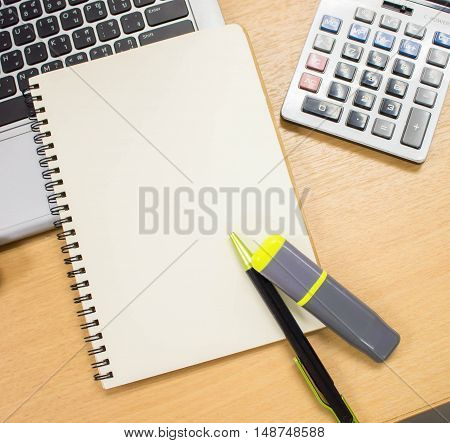 the office table desk with book,pen,calculator,laptop. the blank paper of book is use for putting some texts or images.