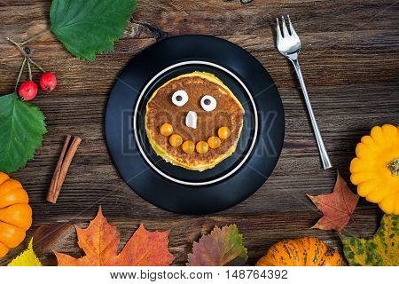 Pumpkin Halloween pancake for kids on black plate on wooden table. Overhead view, horizontal