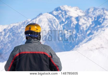 Man in black coat and yellow helmet watch on mountain peaks on ski resort. Winter extreme sport concept. Copy space for advertising.