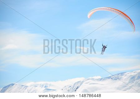 Paragliding high in mountains in blue bright sky. Tandem fly above peaks snowy peaks in sunny day. Extreme sport life.