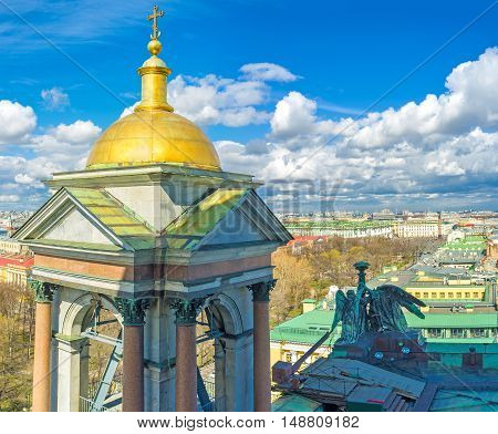 The golden domed bell tower of St Isaac's Cathedral with its bronze sculptures and St Petersburg skyline on the background Russia.