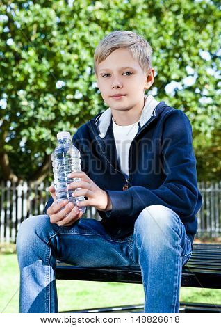 Young teenage boy with bottle of water in park sitting on the bench