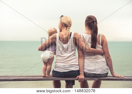 Loving mother embracing her children sitting on wooden bench at tropical beach during vacation. They together looking into the distance. Concept for togetherness and  bright future.