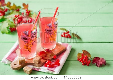 Fresh viburnum drink in glass on green wooden background with leaves and berries. Selective focus.