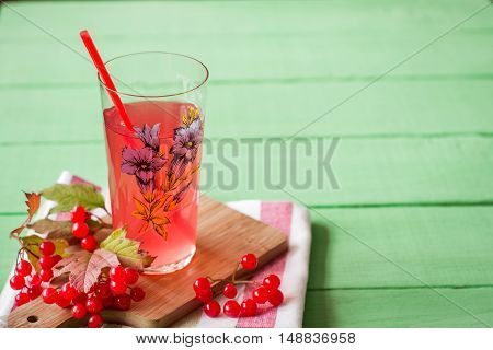 Fresh viburnum drink in glass on green wooden background with leaves and berries. Selective focus.