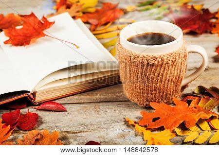 Hot drink in a large cup, book, colorful autumn leaves on a wooden table surface
