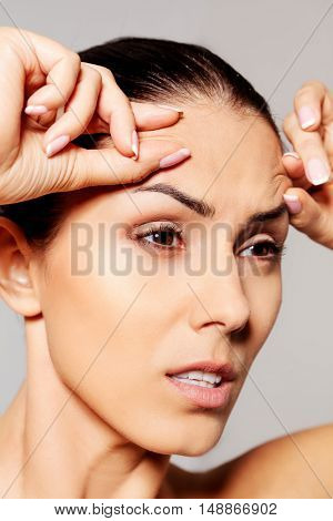 Worried young woman checking wrinkles on forehead