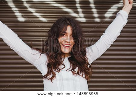 Woman smiling with perfect smile and white teeth over urban wall with hands rasied