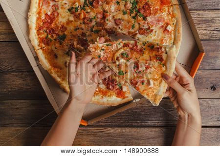Female Hands Taking Slice Of Pizza On Wooden Table