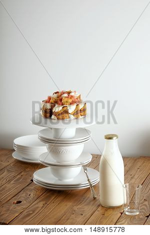 Nontraditional wedding cake with cream, chocolate and grapefruit balanced on a pyramid of white cups and saucers with a bottle of milk next to it