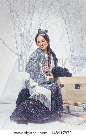 Beautiful young woman with russian national traditional shawl sitting on sled. Snowfalkes. Copy space.