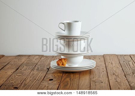 Similar but different white t-cups perched on top of each other with a tiny bit of light brown sponge cake on a saucer