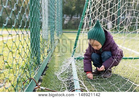 Little girl playing on a fooball pitch. She is sitting behind the goal.