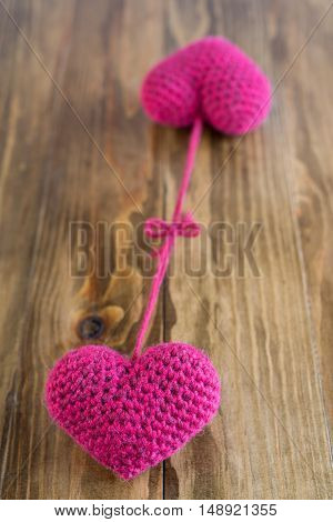 Two chrocheted hearts tied together on a wooden background. Soft focus on a nearest heart.
