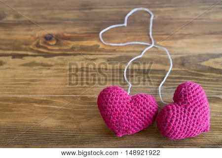 Two chrocheted hearts with threads on a wooden background. Soft focus on hearts.