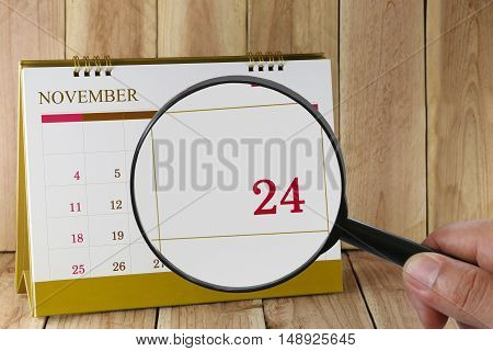 Magnifying glass in hand on calendar you can look Twenty-four days of monthFocus number Twenty-four in NovemberConcept in business and meetings.