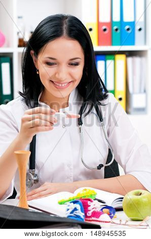 Smiling medical nurse with holding positive pregnacy test. Portrait of happy young doctor at office. Beautiful young woman doctor sitting at the desk in hospital. 
