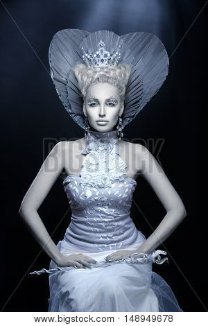 Portrait of beautiful young woman dressed as winter queen. Creative makeup. Over dark background. Copy space.