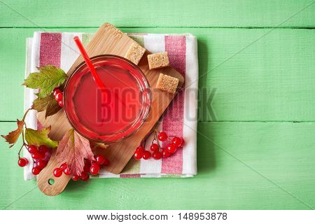 Fresh viburnum drink in glass on green wooden background with leaves and berries. Top view.