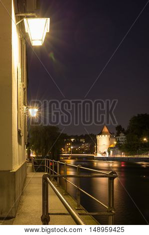 Lights shining on a deserted walkway overlooking the tranquil water of the lake at night Lucerne Switzerland with the city visible in the background