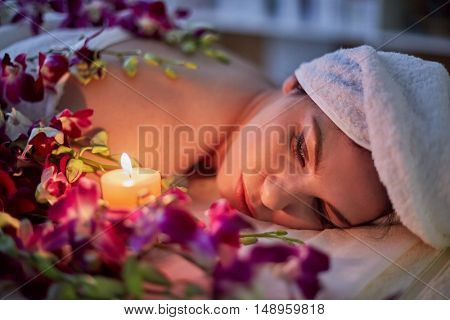 Woman lies on couch with flowers lit by burning candle in beauty salon.