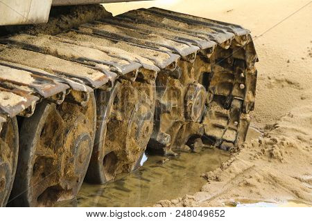 Old Iron Caterpillar In Wet Sand. Rusty Steel Wheels And Caterpillar Tape Of A Large  Bulldozer, Tan