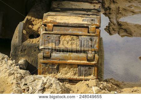 Old Iron Caterpillar In Wet Sand. Rusty Steel Wheels And Caterpillar Tape Of A Large  Bulldozer, Tan