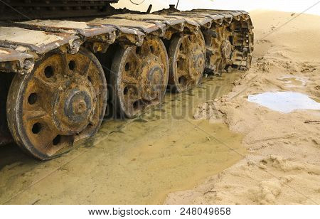 Old Iron Caterpillar In Wet Sand. Rusty Steel Wheels And Caterpillar Tape Of A Large  Bulldozer, Tan