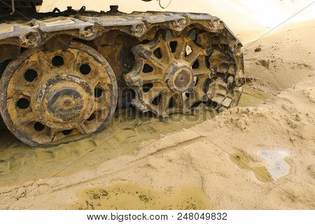 Old Iron Caterpillar In Wet Sand. Rusty Steel Wheels And Caterpillar Tape Of A Large  Bulldozer, Tan