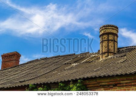 The Roof, Covered With Old Slate, With Old And New Chimneys Made Of Bricks Against The Background Of
