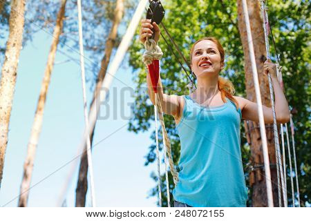 Unusual Experience. Cheerful Young Woman Climbing Down The Trail At A Rope Park While Spending A Wee