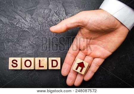 realtor's hand puts a cube with a picture of the house to the word sold. Concept of selling a house, apartment, real estate. market of immobility. Trade of property. Affordable housing. Hand in suit.