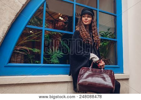 Stylish Young Woman Posing Against Blue Window Outdoors. Fashionable Outfit. Beautiful Model With Cu