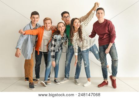 Group of cute teenagers standing near white wall