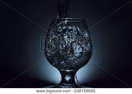 Simple Still-life Photo Of Whisky Glass, Water Jet And Dim Colour Light