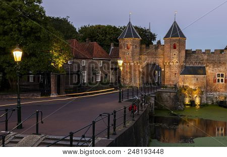 Koppelpoort In The Evening With Lighted Lamp Posts And Bikes At The Old Monument.