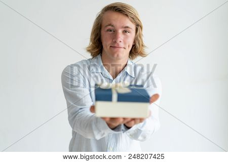 Cheerful Smiling Guy Offering Present Box. Long Haired Blonde Caucasian Man In White Shirt Holding G
