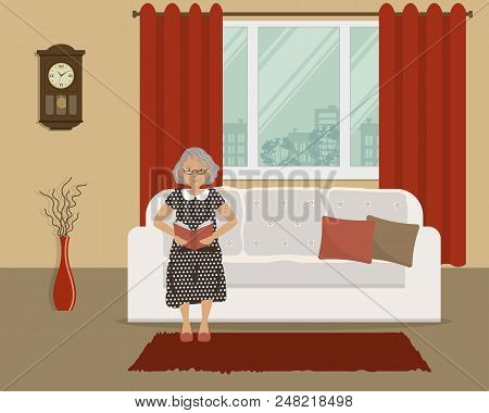 Elderly Lady Is Sitting On The Couch And Reading A Book. There Is A White Sofa On The Window Backgro