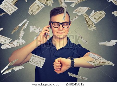 Busy Businessman Looking At Wrist Watch, Talking On Mobile Phone Under Cash Rain. Time Is Money Conc